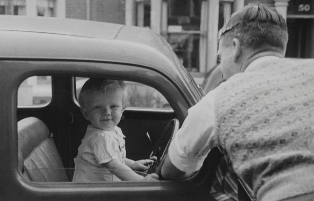 Fekete-fehér fényképen egy kisfiú autót vezet